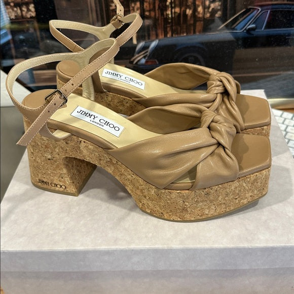 Beige sandal with cork platform and knot detail on a white surface, with blurred background. Luxury for Less