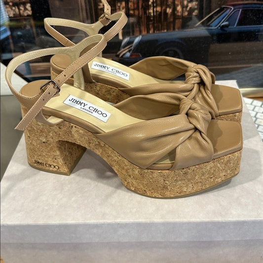 Beige sandal with cork platform and knot detail on a white surface, with blurred background. Luxury for Less